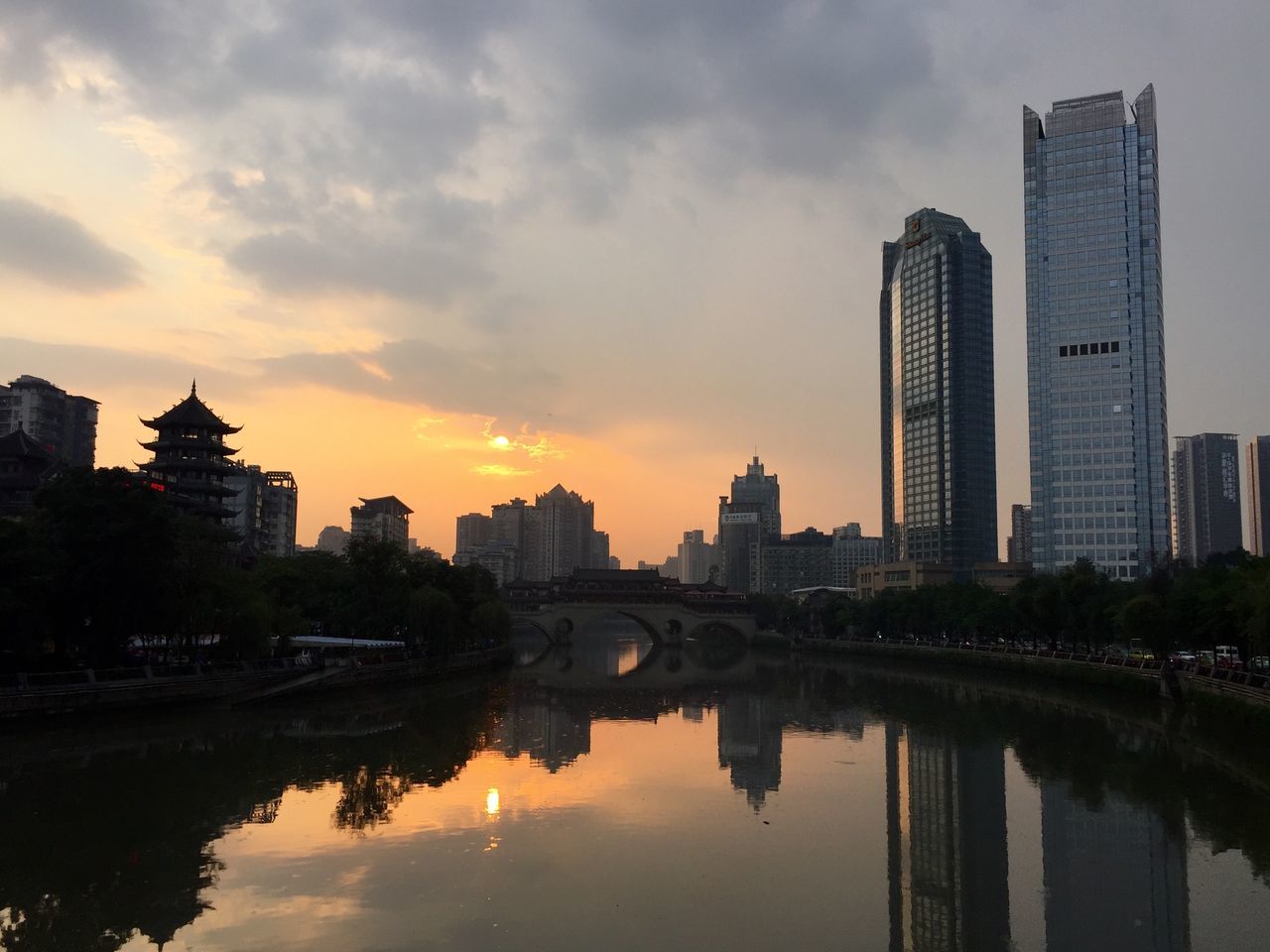 architecture, built structure, building exterior, reflection, water, city, waterfront, sky, sunset, river, connection, skyscraper, cityscape, cloud - sky, bridge - man made structure, building, tower, tall - high, modern, canal