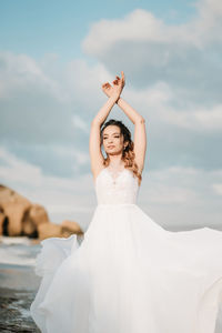 Portrait of woman with arms raised against sky