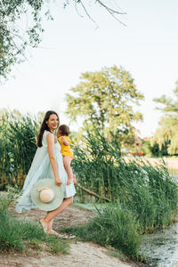 Woman carrying baby while standing against plants