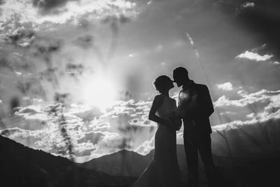 Bride and groom kissing by mountains against dramatic sky