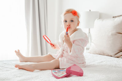 Portrait of cute girl applying make-up while sitting on bed at home