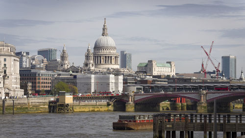 Bridge over river in city against cloudy sky