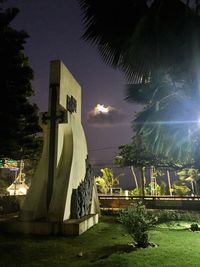 Statue by palm trees against sky at night