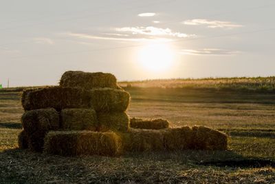 Hay bales on field against sky during sunset
