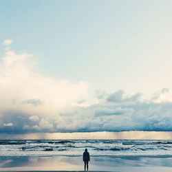 Rear view of woman standing at beach against sky