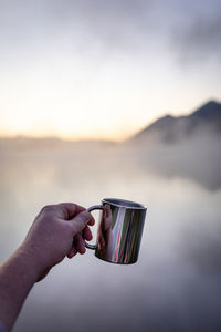 Midsection of person holding coffee cup against sky