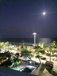 Illuminated lights by sea against sky at night