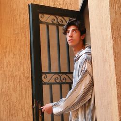 Young man looking away while standing against door