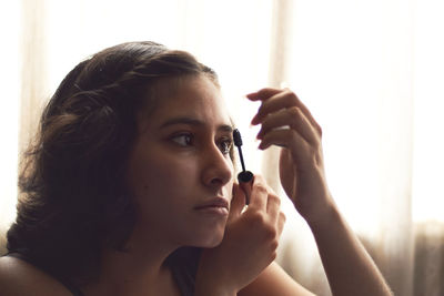 Portrait of young woman putting on makeup, with sun behind