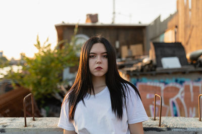 Portrait of beautiful young woman standing by retaining wall on rooftop