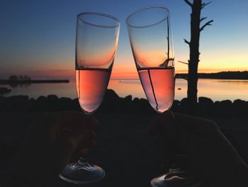 Cropped image of silhouette people tossing champagne flute during sunset