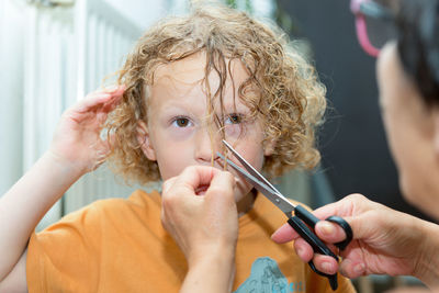 Woman cutting hair of boy with scissors