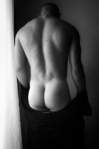 Rear view of shirtless man standing against wall