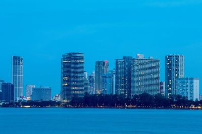 Sea by illuminated cityscape against blue sky