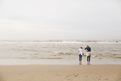 Rear view of women standing at shore against sky