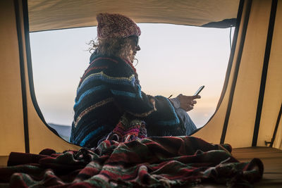 Woman sitting in tent against sky during sunset