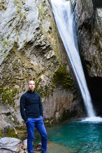 Portrait of man standing on rock against waterfall