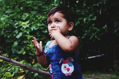 Cute girl sucking finger while standing against plants