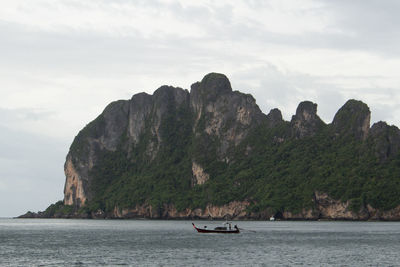 Boat on sea by cliff against sky