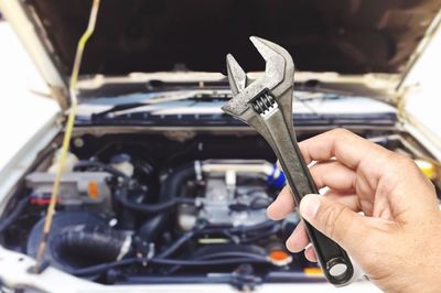 Cropped hand holding spanner against car at garage