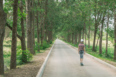 Rear view of man walking on road amidst trees in forest