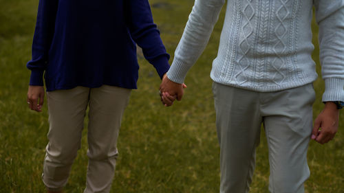 Midsection of couple holding hands while standing on grass 