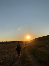 Rear view of man walking on field against sky during sunset