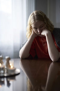 Pensive teenage girl sitting at table with hand on chin