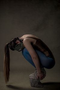 Side view of woman wearing gas mask crouching against gray background