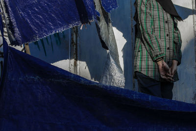 Midsection of woman standing by wall and tarpaulin