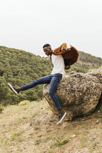 Trendy african american male model in fashionable outfit jumping from stone in highlands