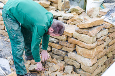 Side view of man picking up stones while standing by retaining wall