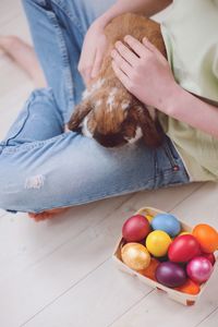 Low section of woman with bunny sitting by easter eggs at home