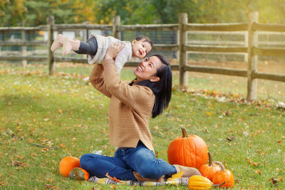 Mother picking up daughter while sitting on land during autumn