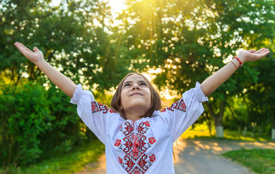 Girl looking up with arms raised against trees