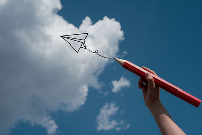 Digital composite image of hand drawing airplane against sky