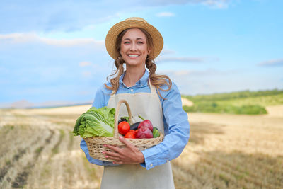 Portrait of smiling young woman standing in basket on field