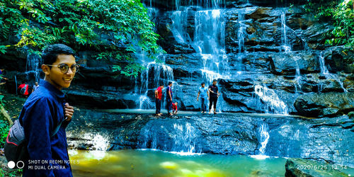 People standing on rock against waterfall