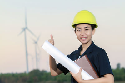 Portrait of engineer holding blueprint against sky