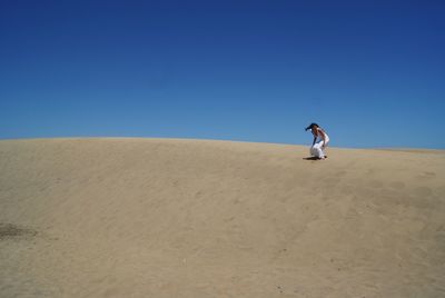 Low angle view of young woman sandboarding against clear blue sky at desert