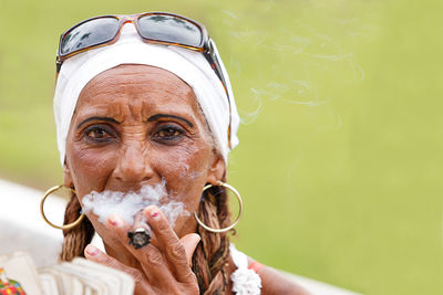 Portrait of woman holding playing cards and smoking cigar while sitting outdoors