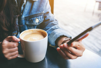 Midsection of businesswoman using smart phone while holding coffee cup at cafe