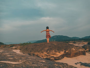 Rear view of man standing on rock against sky