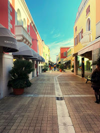 Sidewalk by buildings in city against sky