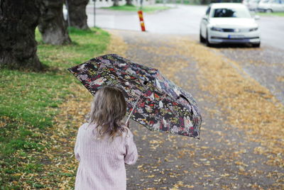 Rear view of girl holding umbrella while standing on road during autumn