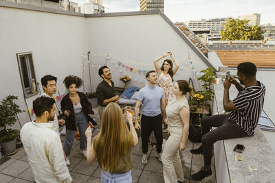 Young man photographing male and female friends dancing on rooftop deck at party