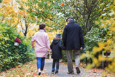 Full length rear view of boy walking with great grandfather and mother in park during autumn