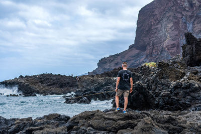 Rear view of man standing on rock against sky