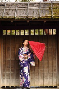 Woman in traditional clothing with umbrella standing against wall