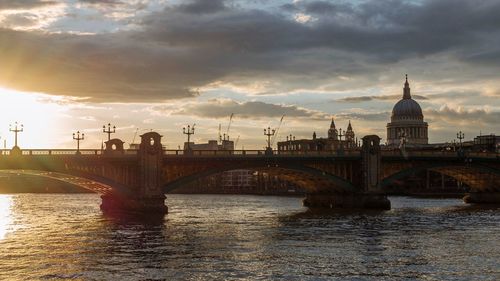 Bridge over river in city against cloudy sky